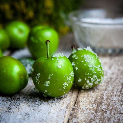 Grüne Pflaumen mit Salz Pflanzenseitenansicht auf einem Holztisch