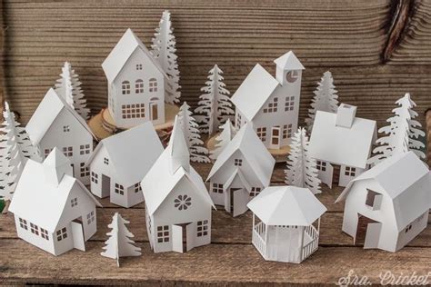 Small White Paper Houses Sitting On Top Of A Wooden Table Next To Pine