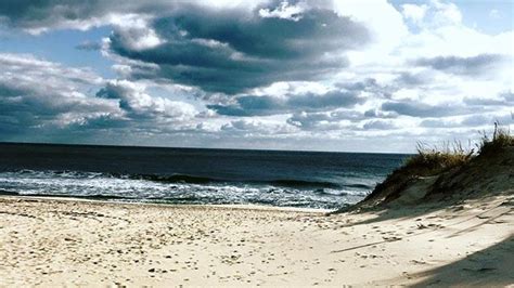 a sandy beach with waves crashing on the shore and dark clouds in the ...