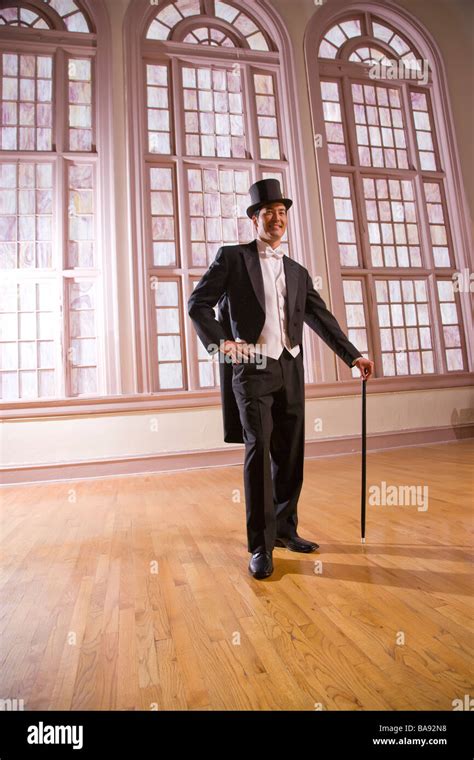 Man In Tuxedo With Top Hat And Cane Standing In Ballroom Stock Photo