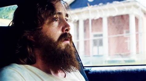 a man sitting in the back seat of a car with a long beard and wearing a white t - shirt