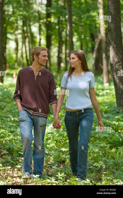 Full Body Portrait Of Young Couple Walking Hand In Hand Through Forest