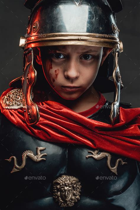 Roman Preschool Boy In Dark Armour With Red Cloak In Dark Background