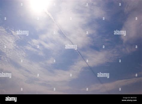 A condensation trail of a jet airplane against a blue sky with clouds ...