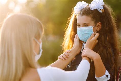 Mãe carinhosa ajuda a usar máscara médica estudante ao ar livre escola