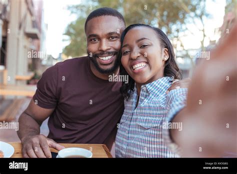 Smiling Young African Couple Taking Selfies Together At A Cafe Stock