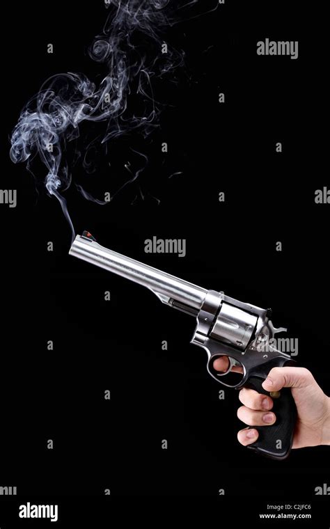 hand holding a revolver with smoking barrel, against black background ...