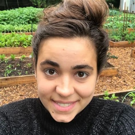 A Woman With A Messy Topknot Is Smiling At The Camera In Front Of Her