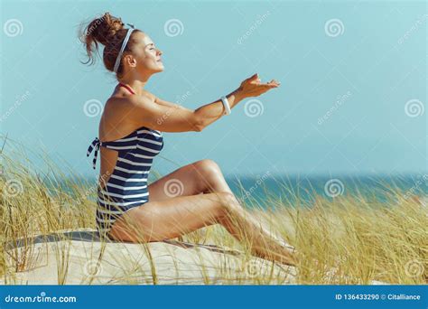 Relaxed Woman Sitting With Hands Stretched Forward On Seacoast Stock