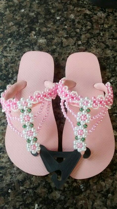 A Pair Of Pink Flip Flops With Pearls And Beads On The Toes Sitting On