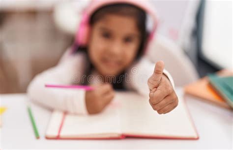 Adorable Hispanic Girl Student Sitting On Table Drawing On Notebook