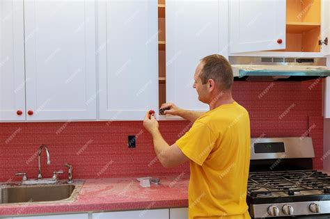 Premium Photo | Worker installs doors to kitchen cabinet installation ...