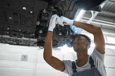 Male Auto Mechanic Working Under Car Lifted On Elevator With Flashlight