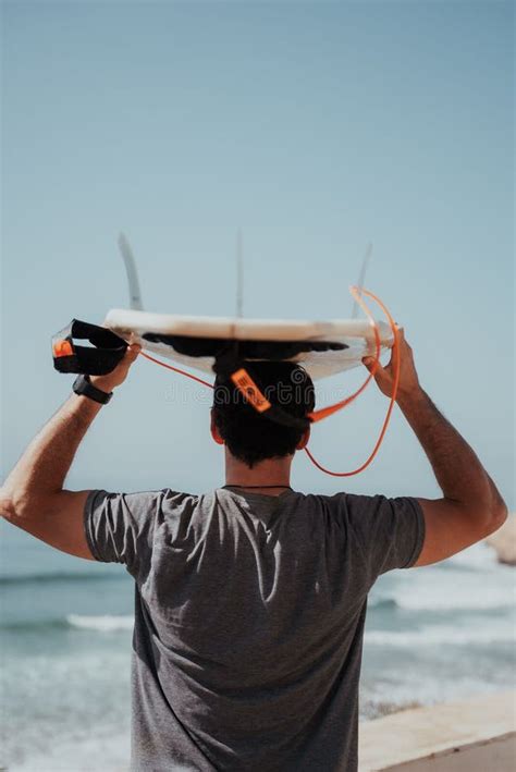 Vertical Shot Of A Man Carrying A Surfboard Over His Head On A Beach