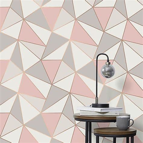 a pink and grey geometric wallpaper with a lamp on the table next to it