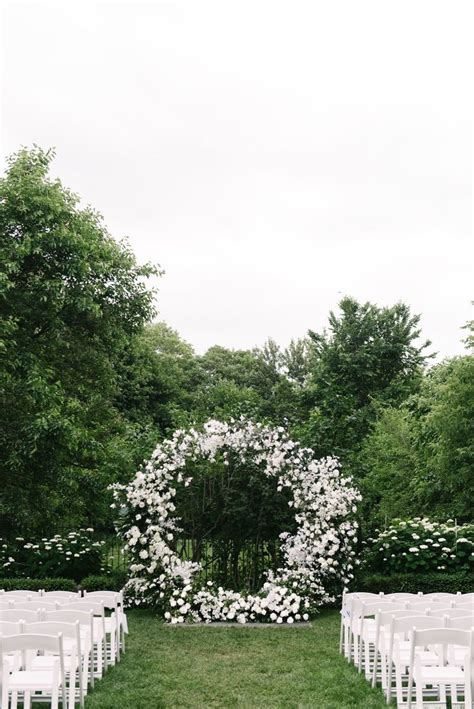 An Outdoor Ceremony Setup With White Chairs And Flowers