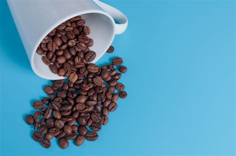 Premium Photo Coffee Beans Spill Out Of A White Cup On A Turquoise