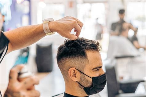 Barbero poniendo laca en el cabello de un hombre caucásico con una