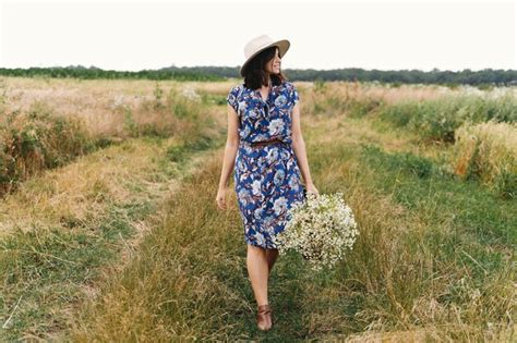 Élégante jeune femme en robe vintage bleue et chapeau marchant avec des