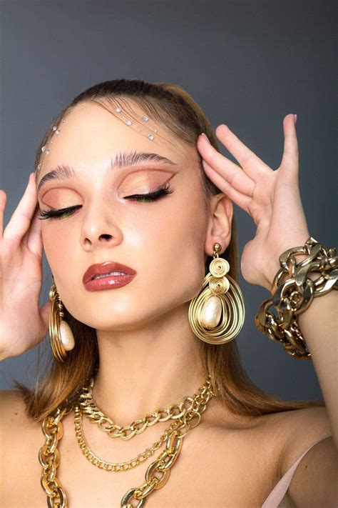 A Woman Wearing Gold Jewelry And Holding Her Hands Up To Her Face