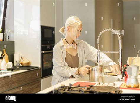 Mature Woman Filling Steel Jug With Water In Kitchen At Home Stock