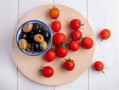 Vista superior de azeitonas verdes e pretas na tigela e tomate na tábua