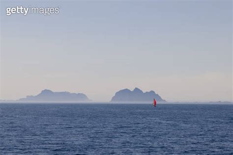 A Solitary Sailboat With A Vivid Red Sail Glides Through The Placid