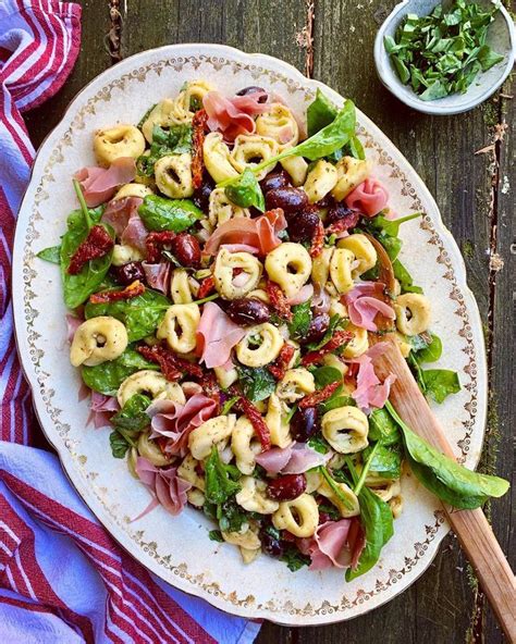 A Plate With Pasta Salad On It Next To A Bowl Of Greens And A Wooden Spoon