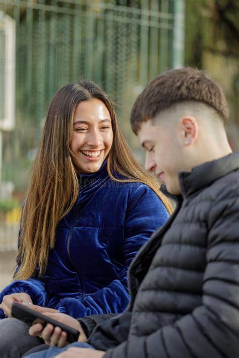 Latina Girl Smiling Sitting On A Plaza Bench With Her Boyfriend Stock Photo Image Of Cellphone