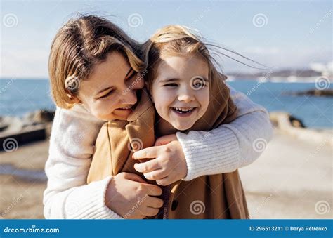 A Smiling Mother Hugs Her Cute Laughing Daughter On The Seashore A