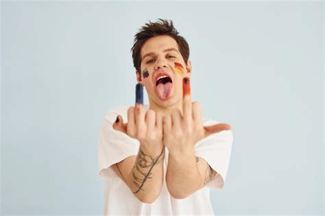 Joven gay está parado en el estudio y posando para una cámara muestra los dedos medios Foto