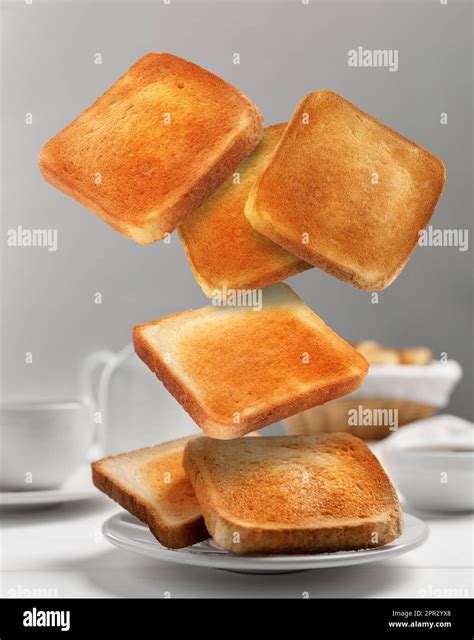 Delicious Toasted Bread Falling Into Plate On White Table Stock Photo