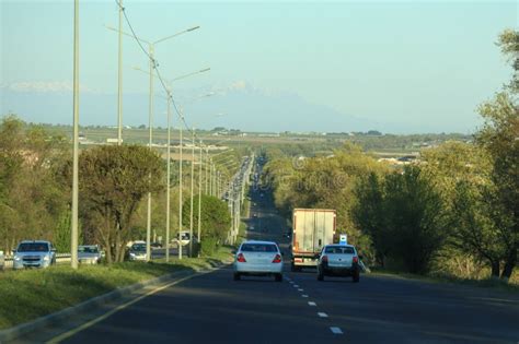 A Long Four-lane Highway with Busy Traffic with a Row of Street Lights among the Trees in the ...