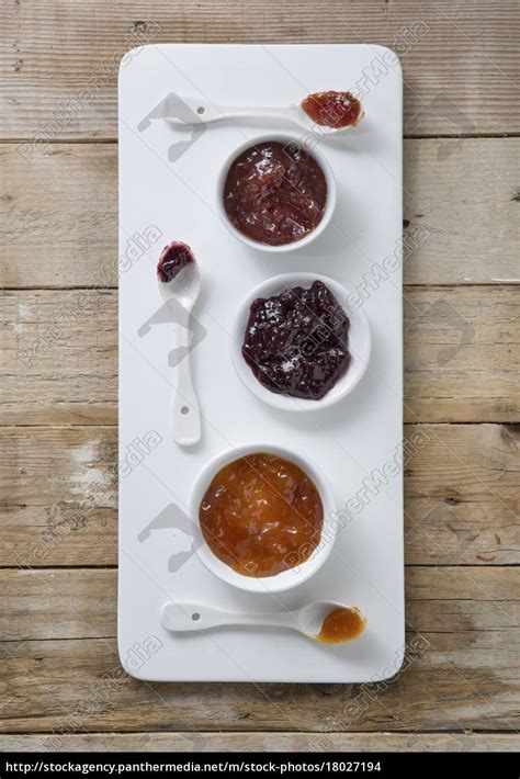 Three Types Of Jam In Bowls With Spoons On A Board Stock Photo