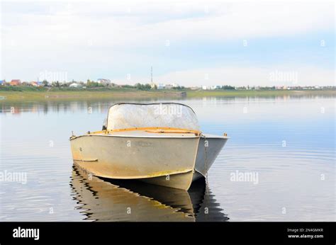 Old Metal Boat Is In Calm Water With Reflection Of Clouds Was Chained