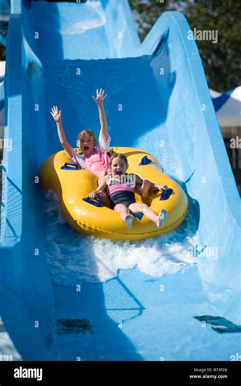 Two Young Girls Sliding Down Water Slide Together On Innertube In Water