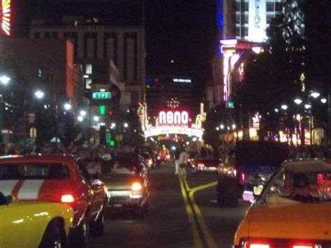 Cars Driving Down The Street At Night With Neon Signs And Buildings In