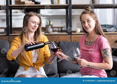 Two Lesbians Holding Wine Glasses And Pouring Wine While Sitting On