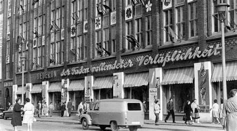 An Old Black And White Photo Of People Walking On The Sidewalk In Front