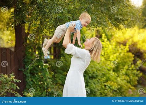 La Blonde De Maman Dans La Robe Blanche Soulève Le Petit Garçon Et L a Riant Image stock Image