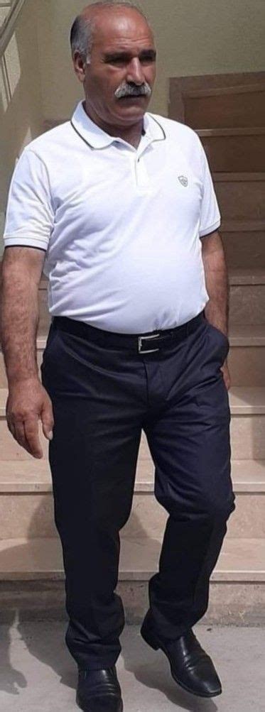 A Man With A Moustache Standing In Front Of Stairs Wearing Black Pants