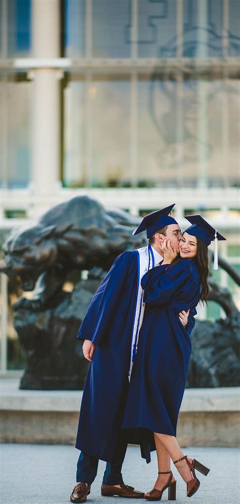 Two Graduates Hugging Each Other In Front Of A Statue And Fountain At