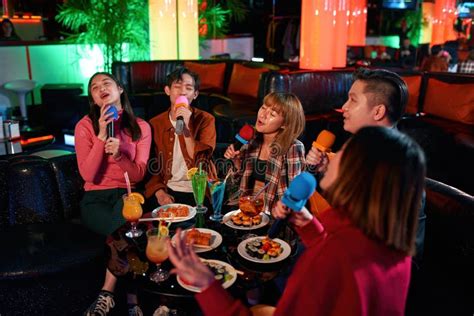 Group Of Asian Friends Having Fun And Singing Songs At Karaoke Club