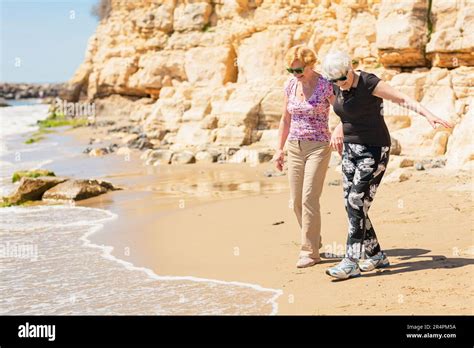 Two Senior Women Walking Along The Rocky Seashore And Playing With The