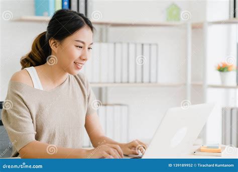 Beautiful Young Smiling Asian Woman Working Laptop On Desk In Living