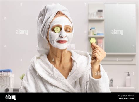 Mature Woman With A Towel On Her Head And A Face Mask Putting Cucumber