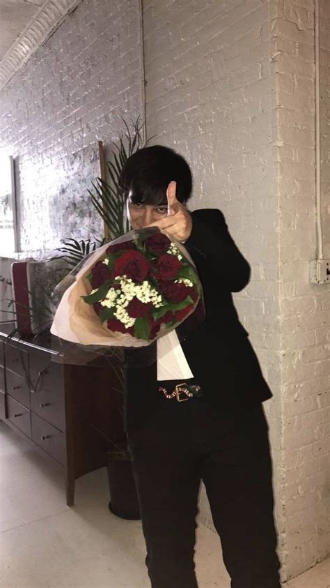 A Man In A Suit Holding Flowers And Giving The Peace Sign