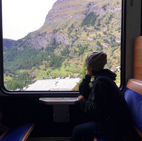 A Person Sitting On A Train Looking Out The Window With Mountains In