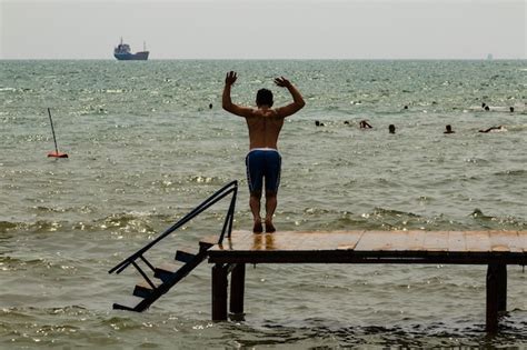 Premium Photo Rear View Of Shirtless Man Jumping Into Sea Against Sky