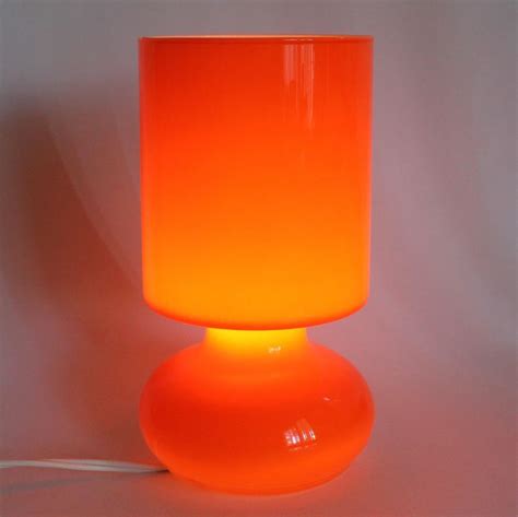 An Orange Lamp Is Lit Up On A White Surface With A Cord Attached To It